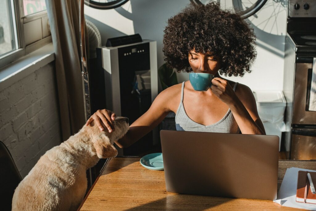 woman with dog sipping coffee while checking her laptop